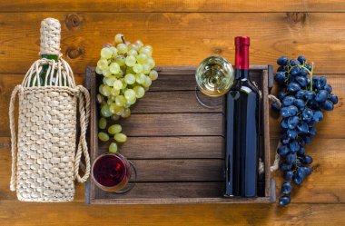 İki şişe ve bardak kırmızı ve beyaz şarap ve üzüm ahşap arka plan üzerinde. Üstten görünüm, boşluk.