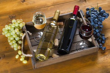 İki şişe ve bardak kırmızı ve beyaz şarap ve üzüm ahşap arka plan üzerinde. Üstten görünüm.