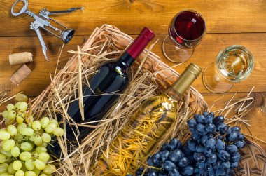 İki şişe ve bardak şarap ile saman, sepetteki ile demetleri üzüm, mantarlar ve bir tirbuşon ahşap arka plan üzerinde. Üstten görünüm.