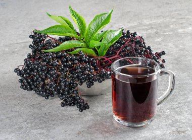 Yeşil yaprakları ve bir bardak içki ile olgun mürver çilek kümeleri.