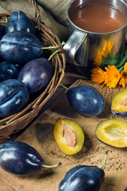 Olgun mavi erik suyu bir demir kupa ve meyve dilimleri kesme tahtası üzerinde bir sepet içinde. Rustik tarzı. Yakın çekim.