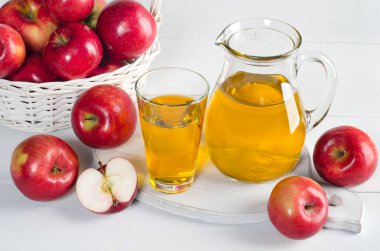 Bir sürahi ve beyaz masada elma ile bir bardak elma suyu