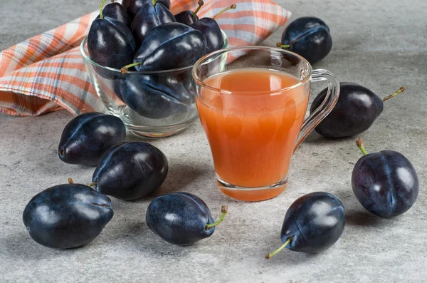 Jus de prune dans une tasse et prunes mûres sur une table grise . — Photo