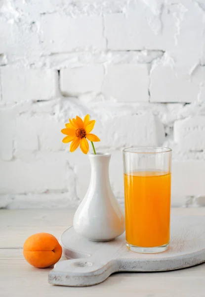 Apricot juice in glass and vase with a flower on wall background — Stock Photo, Image