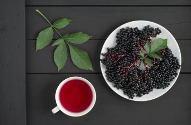 Yeşil yapraklı böğürtlen sürüsü ve ahşap arka planda bir bardak dolusu elderberry. Üst Manzara. Düz yatıyordu.