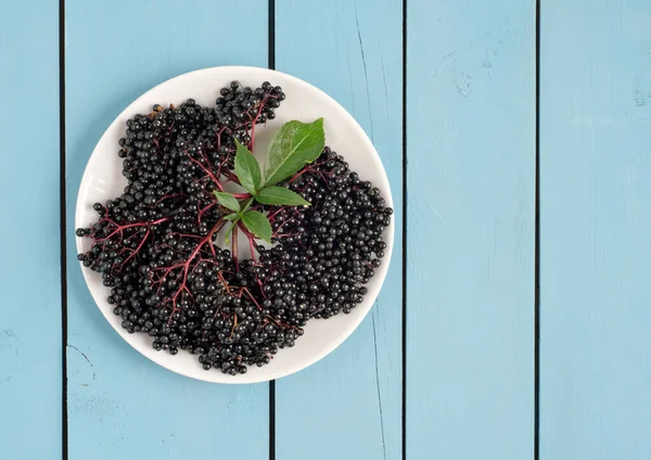 Trauben Von Reifen Holunderbeeren Teller Mit Grünen Blättern Auf Hölzernem lizenzfreie Stockfotos