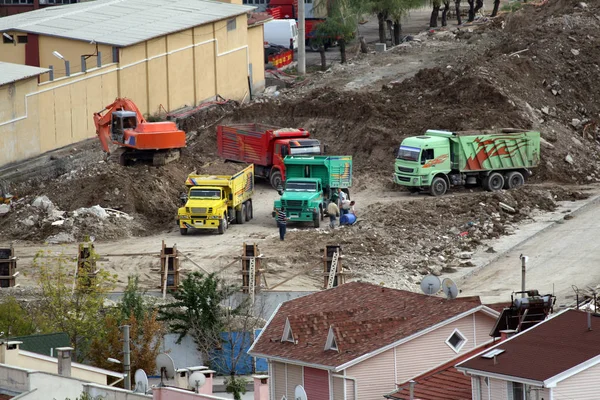 Excavating excavator during construction works loading soil to trucks.