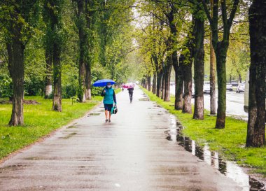 KYIV, UKRAINE - 25 Mayıs 2020. Yağmurlu bir günde bahar sokağı boyunca yürüyen şemsiyeli ve maskeli insanlar..
