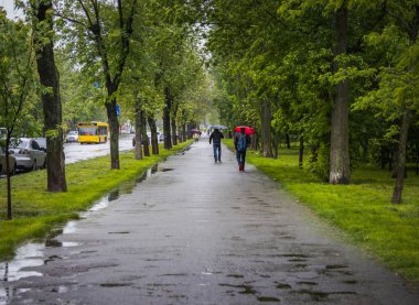 KYIV, UKRAINE - 25 Mayıs 2020. Yağmurlu bir günde bahar sokağı boyunca yürüyen şemsiyeli ve maskeli insanlar..