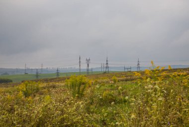 Bulutlu havada elektrik hatları devrede. Sonbahar sahasında elektrik kabloları olan iç karartıcı bir manzara..