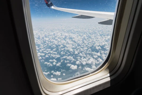 Вид с самолета иллюминатор на крыло самолета, земля под ним и облака летнего дня в полете — стоковое фото