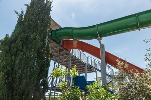 Su parkı. Yeşil, kırmızı ve mavi su kaydırağı. Yeşil ağaçlarla mavi gökyüzü.
