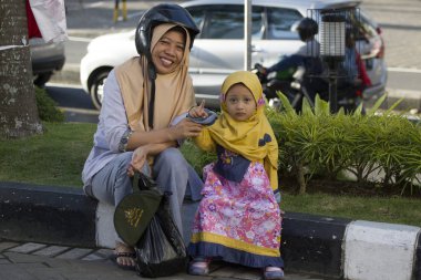 Malang, Java, Indonesie -16 Augustus, 2018: Anne kızıyla birlikte kaldırıma oturur bir kask ile