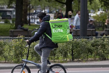 AMSTERDAM, HOLLAND - 16 MEI 2019: Sırtında yeşil bir torbayla bisiklet üstü yiyecek teslimatı