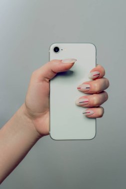 Elinde telefon. Tasarım çivi. El ile matt minimalist manikür ile. Yakın kadar olan kadın el ile Trendy çivi hafif bir arka plan üzerinde. Sanat çivi. Yüksek kaliteli görüntü.
