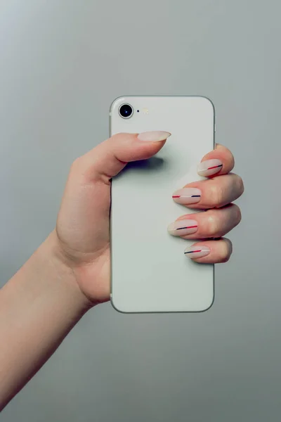 Phone in hand. Nails Design. Hands With with a matt minimalist manicure.  Close Up Of Female Hands With Trendy Nails on a light background. Art Nail. High Quality Image.