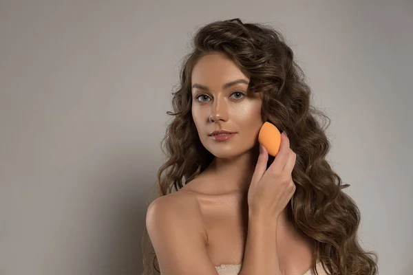 Красивая молодая женщина наносит макияж с помощью губчатого блендера красоты — стоковое фото