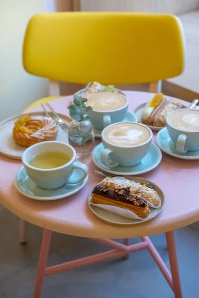 Стол в кафе с чашками кофе, эклерами и тортом — стоковое фото