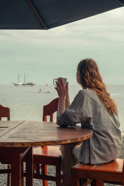 Girl drinks tea and look at the sea