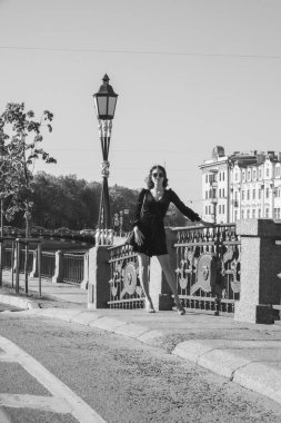 Güzel romantik bir bayanın açık hava portresi. Mükemmel makyaj ve saç stili. Dalgalı saçlı, güneş gözlüklü ve siyah kısa elbiseli bir esmer sahildeki köprüde duruyor..