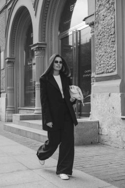 Pantolon giymiş genç bir kadının açık hava moda portresi. Sokak tarzı. Şehrin sokaklarında büyük bir ceket ve güneş gözlüğü takmış esmer bir kadın..
