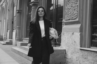 Pantolon giymiş genç bir kadının açık hava moda portresi. Sokak tarzı. Şehrin sokaklarında büyük bir ceket ve güneş gözlüğü takmış esmer bir kadın..