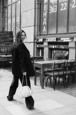 Genç bir kadının açık hava moda portresi. Sokak tarzı. Şehrin sokaklarında büyük bir ceket ve güneş gözlüğü takmış esmer bir kadın..