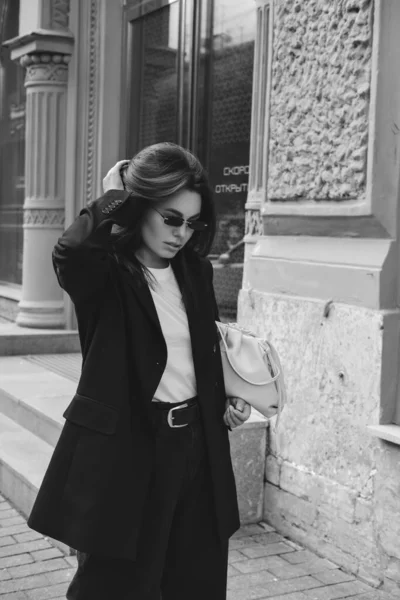 Pantolon giymiş genç bir kadının açık hava moda portresi. Sokak tarzı. Şehrin sokaklarında büyük bir ceket ve güneş gözlüğü takmış esmer bir kadın..