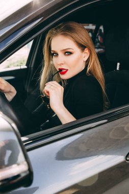 Kırmızı dudaklı genç bayan arabada oturuyor.