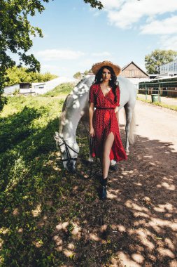 Kırmızı elbiseli, hasır şapkalı, beyaz atlı genç bir kadın. 