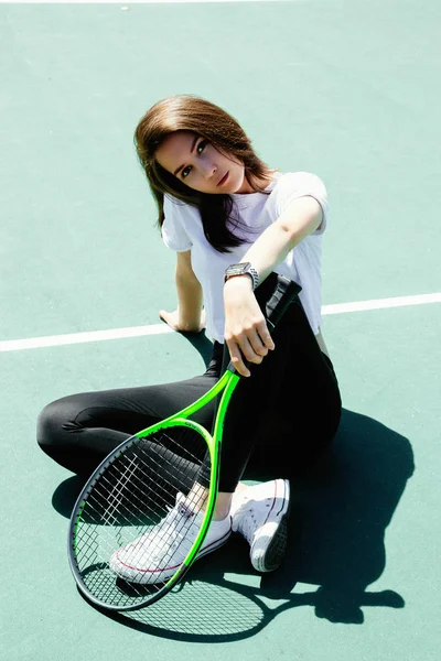 sporty young woman with tennis racket sitting on tennis court