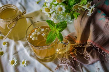 beyaz bir masa örtüsü, ipek eşarp üzerinde papatya ve nane ile çay