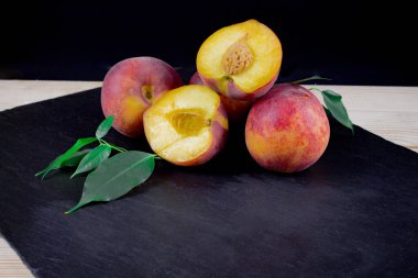 bir kayrak tahtası üzerinde yeşillik ile sulu şeftali, düz yatıyordu, siyah arka plan