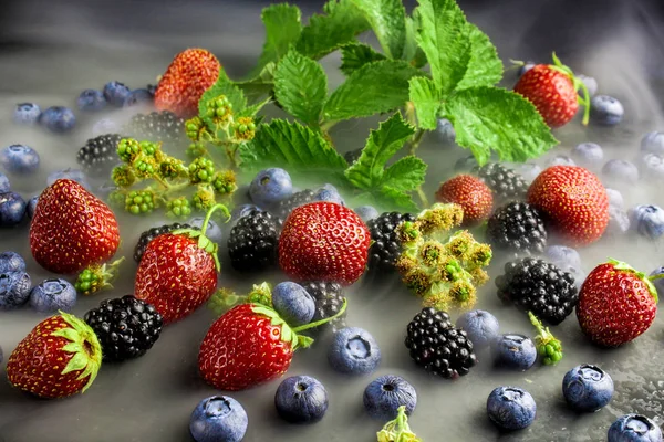 Mix berries on a black background. Blackberries and raspberries with green leaves. Background from berries. Berries in a couple