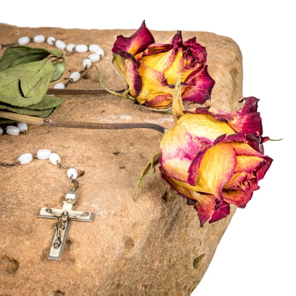 Cruz cristiana en rosario y rosas rojas amarillas secas yacen sobre una piedra arenisca — Foto de Stock