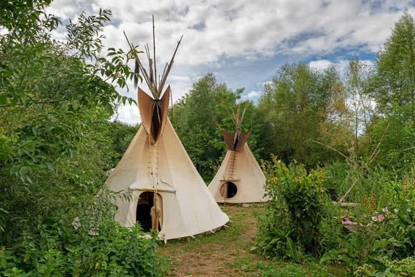 Dwa indyjskie tipi stoją na łące między drzewami i krzewami — Zdjęcie stockowe