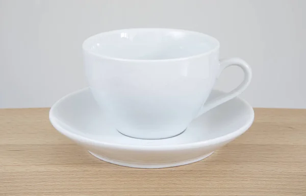 Λευκό κούπα και πιατάκι σε ένα ξύλινο τραπέζι. — Φωτογραφία Αρχείου