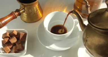 Kahve demsinden sıcak siyah kahve ahşap bir masa üzerinde bir tabak üzerinde beyaz bir porselen fincan içine dökmek için 