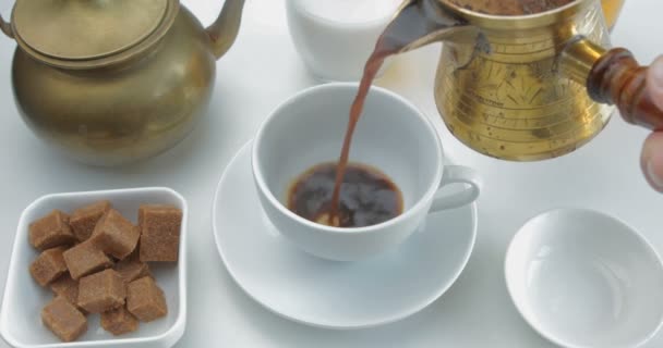 木製のテーブルの上のソーサーの上に白い磁器のカップに注ぐためにコーヒーポットからホットブラックコーヒー — ストック動画