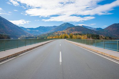 Sylvenstein Gölü üzerindeki köprü, boş yol. Sonbaharda Karwendel dağlarının manzarası. Bulutlu mavi gökyüzü