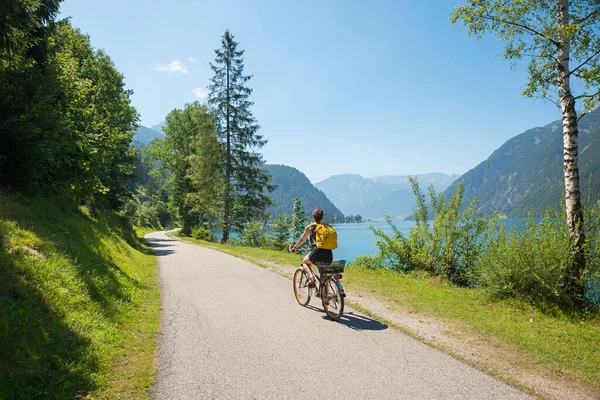 young woman on bike way at lakeside Achensee east with mountain view, landscape tirol austria