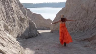 Turuncu elbiseli kız kanyondan göl kıyısına doğru kum dağları arasında koşuyor.