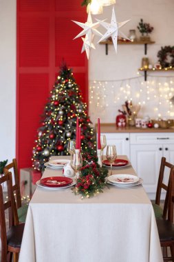 Noel için ağaç, hediye, mum ve sıcak bir tatil ortamı yaratan şenlikli bir yemek masasıyla süslenmiş parlak bir mutfak.