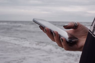 Kız cep telefonu deniz ve gökyüzü arka plan üzerinde tutar.