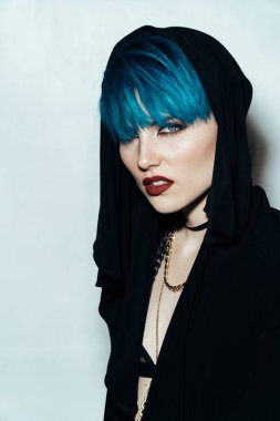 moda fotoğrafçılığı doğrudan kameraya bakarak beyaz zemin üzerine mavi saçlı kız. Kalın sarı zincir ve boynundaki bijouterieher. Profesyonel model Studio poz