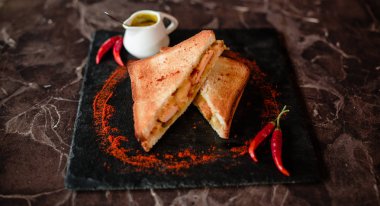 Bir sandviç siyah bir tepsi üzerinde kırmızı biber serpilir. Kalenin yanındaki sosum. Kahvaltı hazır mı