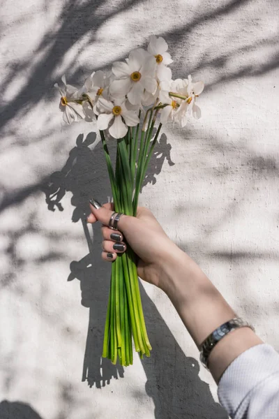 Girl holds flowers in her hand against a white wall with tree shadow