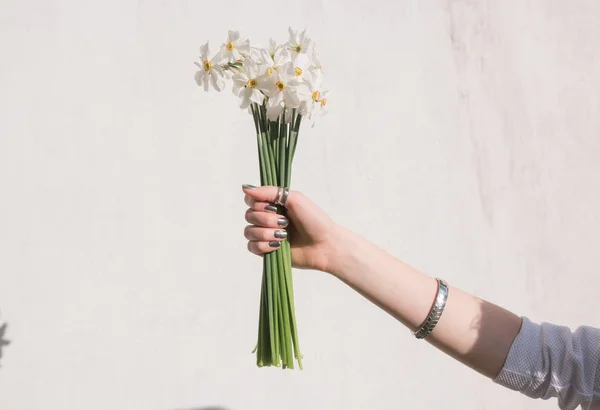 Girl holds flowers in her hand against a white wall with tree shadow