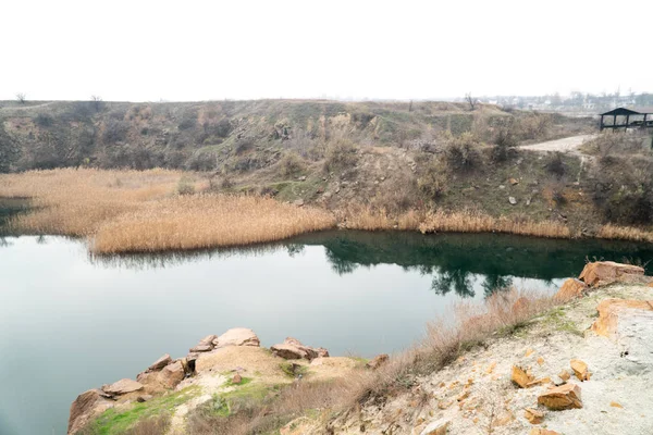 A water-filled quarry with a rocky shore. Sprouted reeds in different places