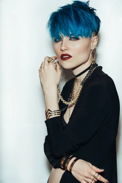 fashion photography of a girl with blue hair on a white background looking directly at the camera. Thick yellow chain and bijouterieher on her neck. Professional model posing in studio